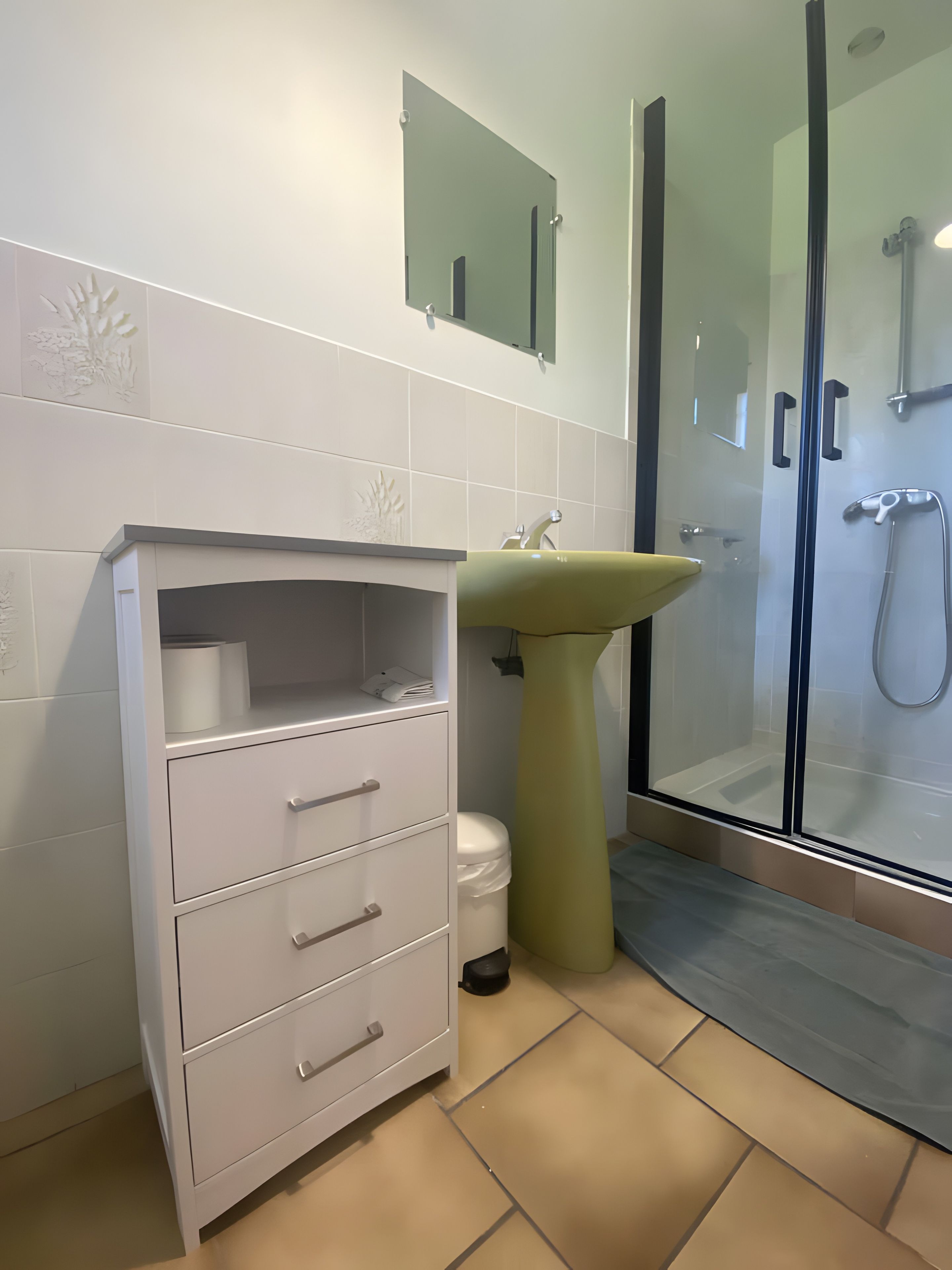 A bathroom with a white vanity, a green sink, and a glass-enclosed shower area.