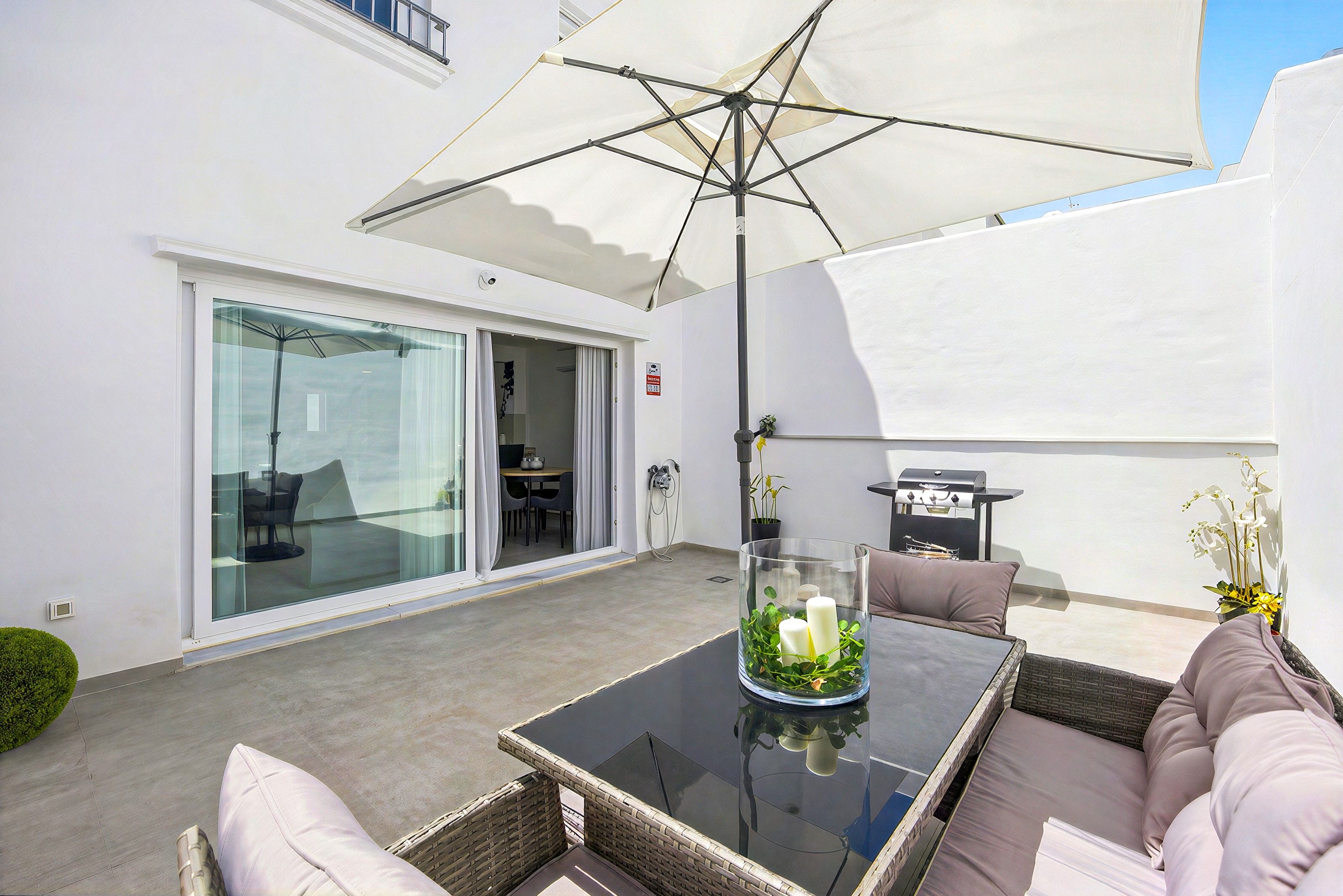 An outdoor patio with a glass door leading to a dining area, a table with cushions, and a grill.