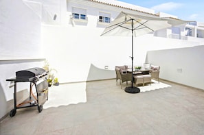 Zona de pati amb una barbacoa, mobiliari exterior i un para-sol gran.