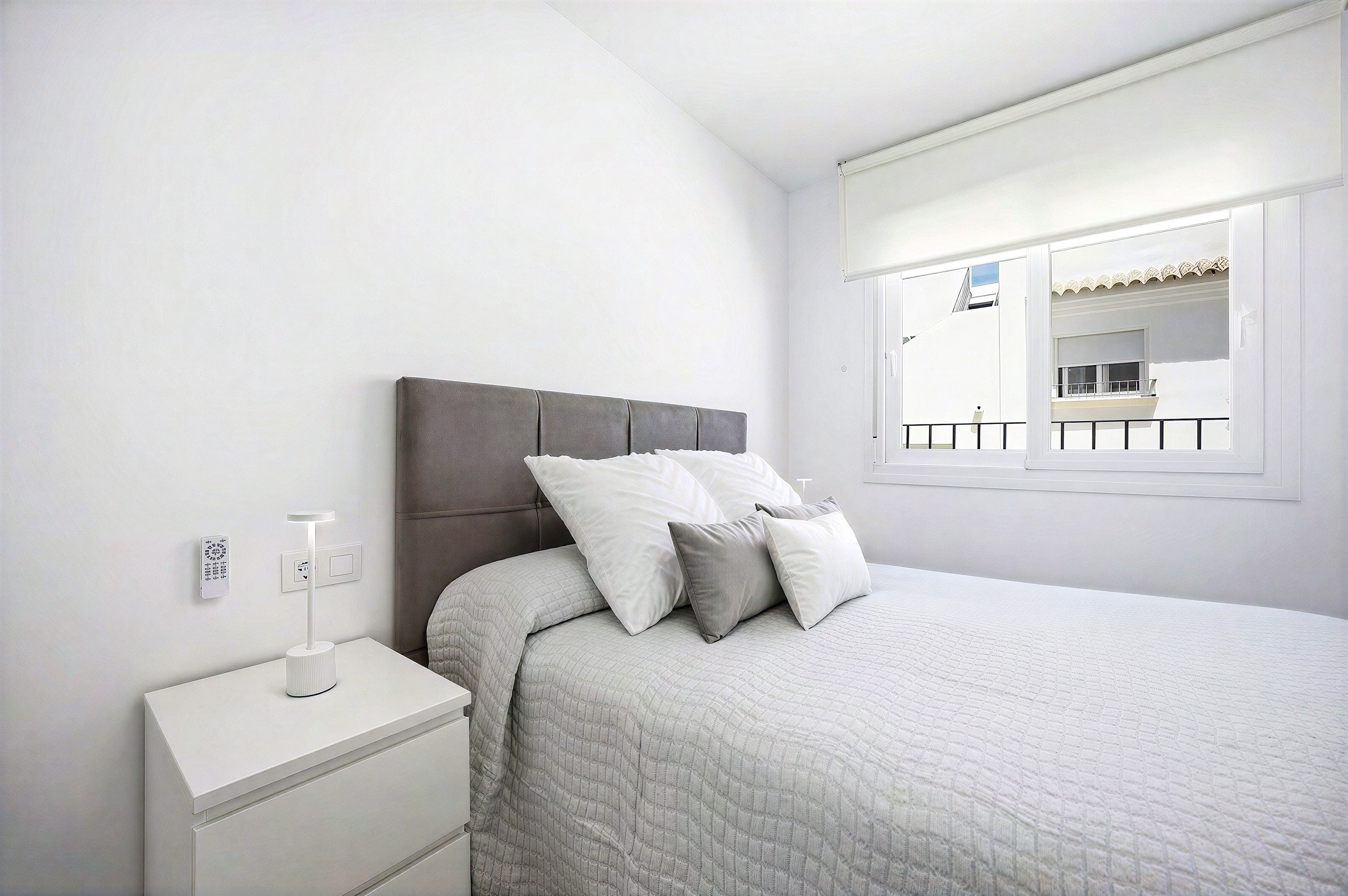 A bedroom with a bed, nightstand, and a window with a view of a balcony.