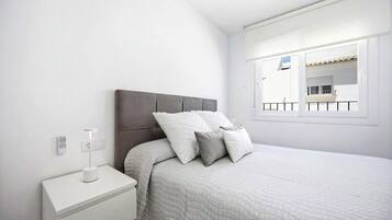 A bedroom with a bed, nightstand, and a window with a view of a balcony.