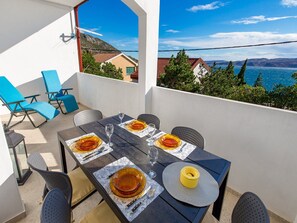 A dining area with a table set for four, outdoor chairs, and a view of the sea and mountains. - Apartments Sun 4 You - Two Bedroom Apartment With Balcony and Sea View (Karlobag)