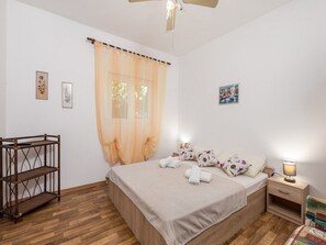 A bedroom with a bed, a wooden shelf, a nightstand, a lamp, and a window with sheer curtains. - Apartments Sun 4 You - Two Bedroom Apartment With Balcony and Sea View (Karlobag)