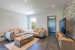 A modern living room with a sofa set, a coffee table, and a flat-screen TV mounted on a stone wall.
