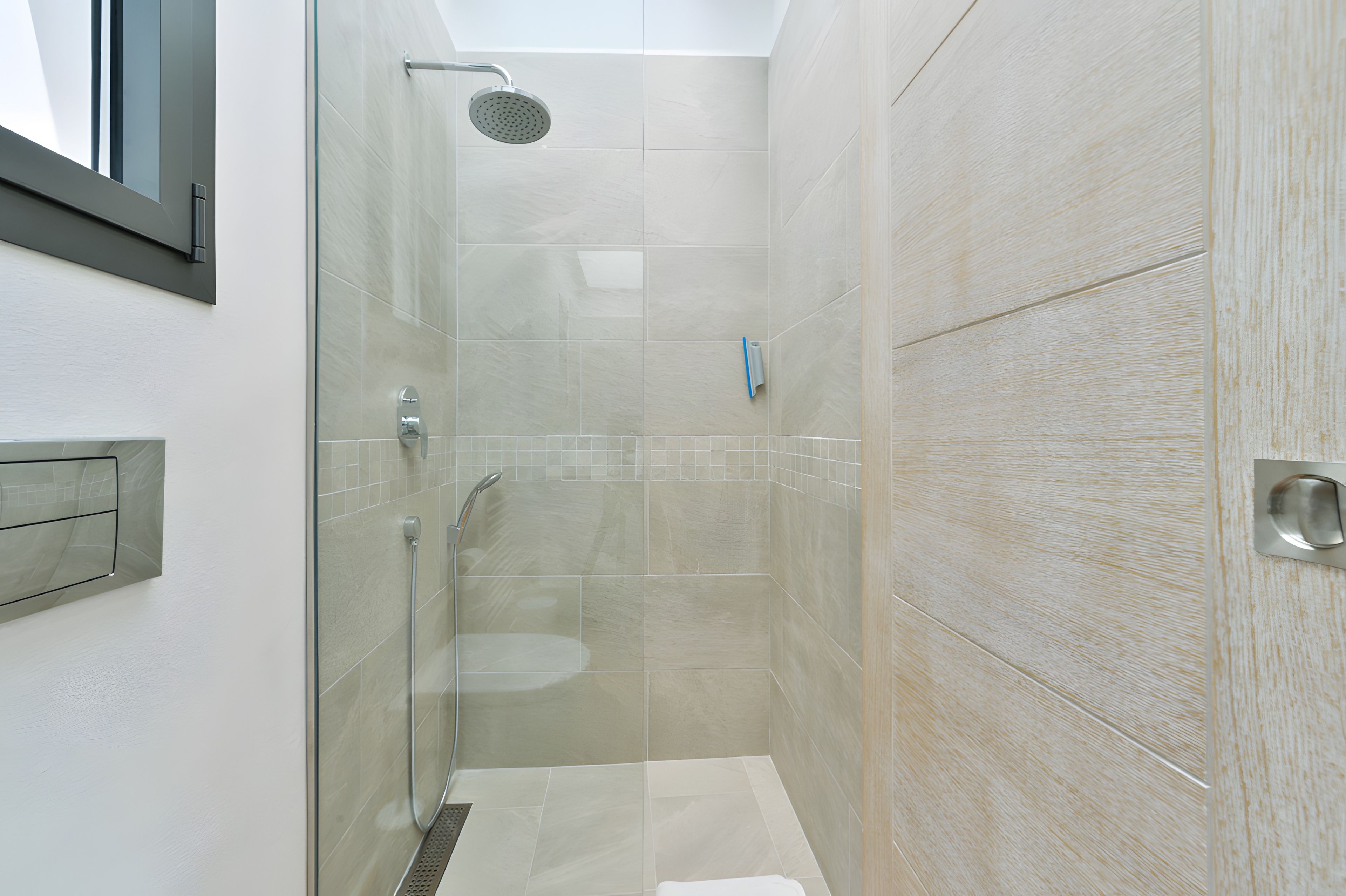 Ducha moderna con puerta de vidrio, cabezal de ducha de mano y panel de control en la pared.