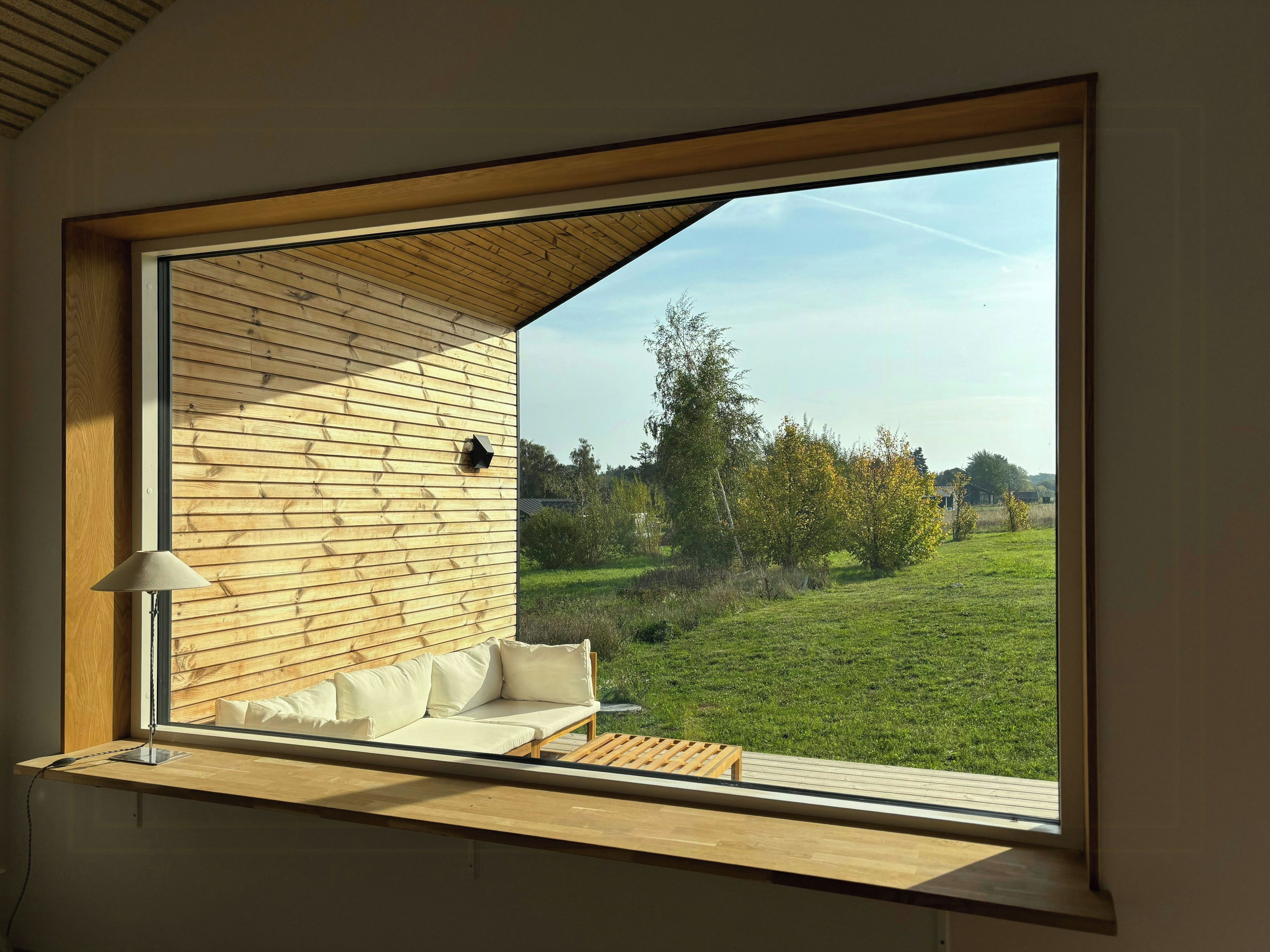 Una habitación con un ventanal grande, paneles de madera en la pared, un sofá y una lámpara.