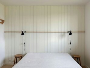 Ein Schlafzimmer mit einem Bett, zwei hölzernen Hocker und zwei Wandlampen.