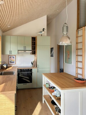 Eine kleine Küche mit hellgrünen Schränken, einer Holz Arbeitsplatte und einer hängenden Pendelleuchte.