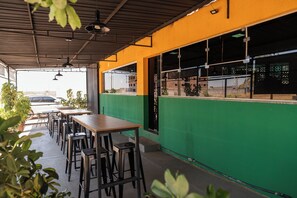 An outdoor seating area with tables and chairs, a green wall, and a view of the street.