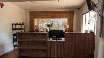 A reception desk with a computer, a potted plant, and a window with blinds.
