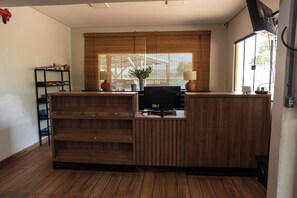 Un comptoir d’accueil avec un ordinateur, une plante en pot et une fenêtre avec des stores.