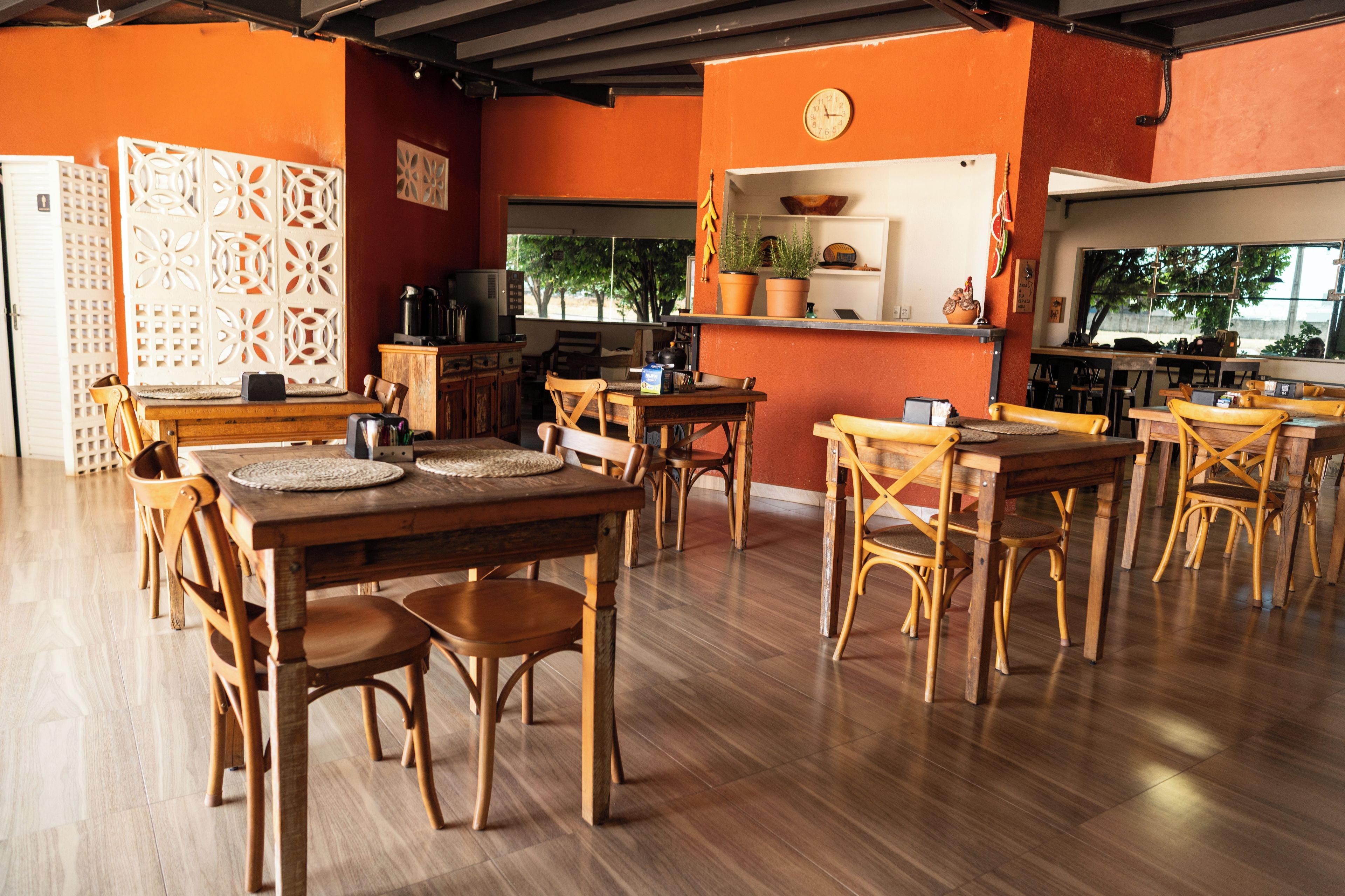 A restaurant with wooden tables and chairs, a kitchen area, and a view through the window.