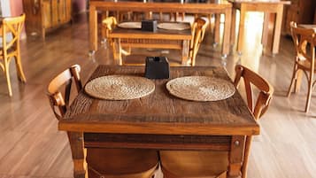 A restaurant with wooden tables and chairs, a red wall with artwork, and hanging lights.