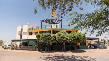 A multi-story building with a balcony, surrounded by trees and parked cars.