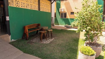 A small outdoor seating area with a bench and two stools, a potted plant, and a green wall with a decorative pattern.