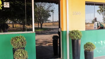 A building with a green and yellow facade, a reception area with a sign, and potted plants in front.