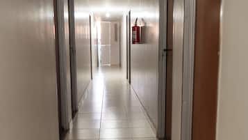A long, narrow hotel corridor with doors on both sides, a fire extinguisher mounted on the wall, and a ceiling light fixture.