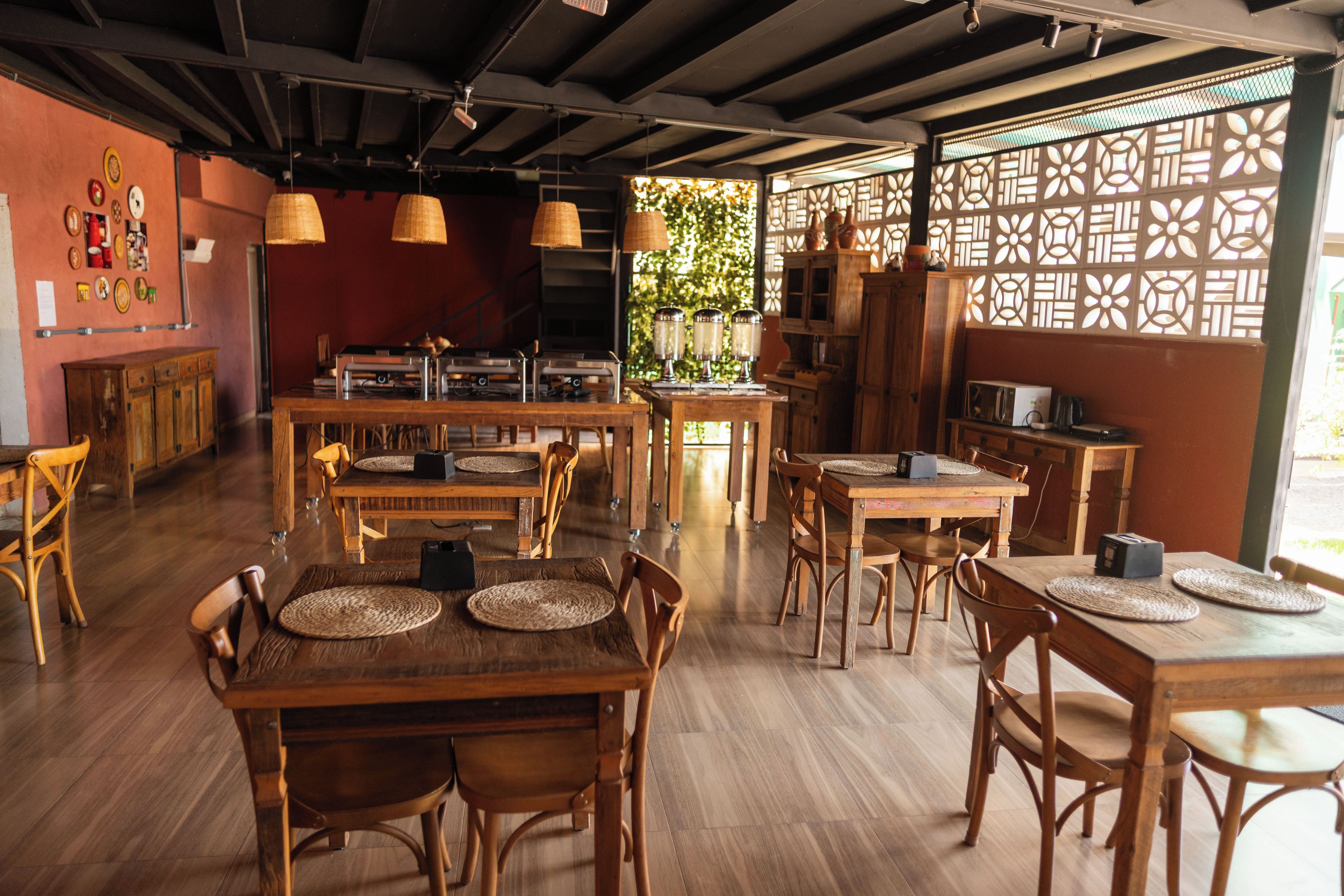 A restaurant interior with wooden tables, chairs, hanging lights, and a decorative partition.
