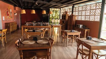 A restaurant interior with wooden tables, chairs, hanging lights, and a decorative partition.
