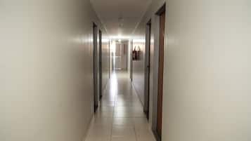 A long, narrow hallway with doors on both sides, leading to a bright room at the end.