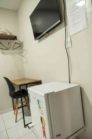 A compact kitchenette with a refrigerator, a small table, and a chair. A flat-screen TV is mounted on the wall above the table.