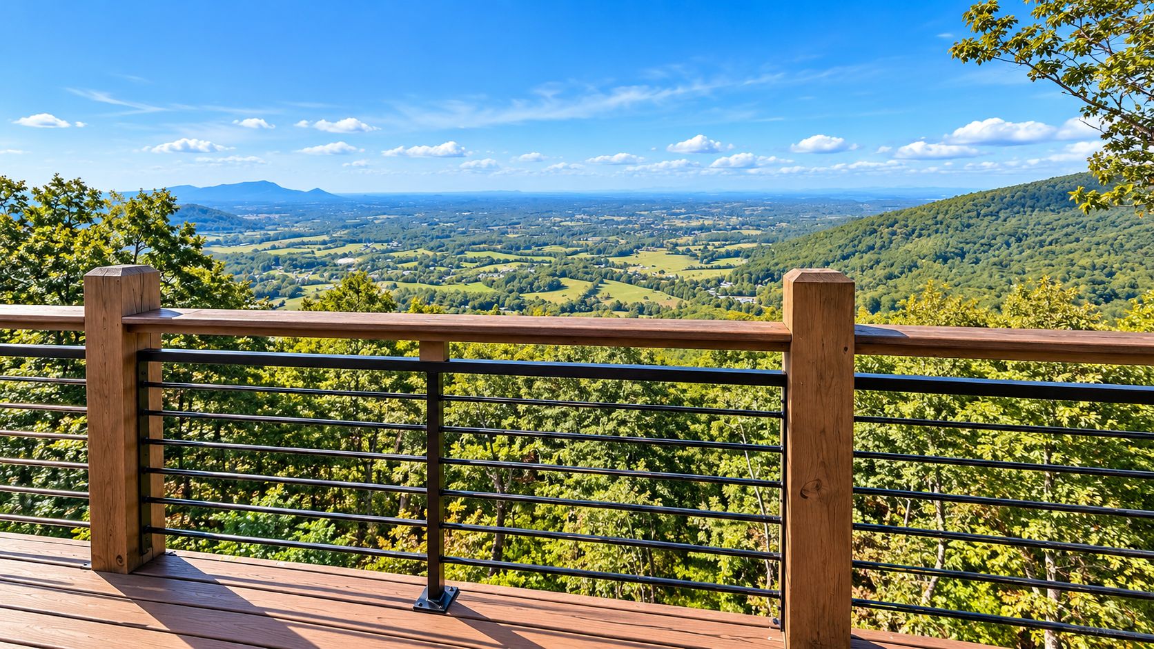 Une terrasse en bois avec une rambarde en métal, donnant sur une vallée verdoyante et des montagnes lointaines.