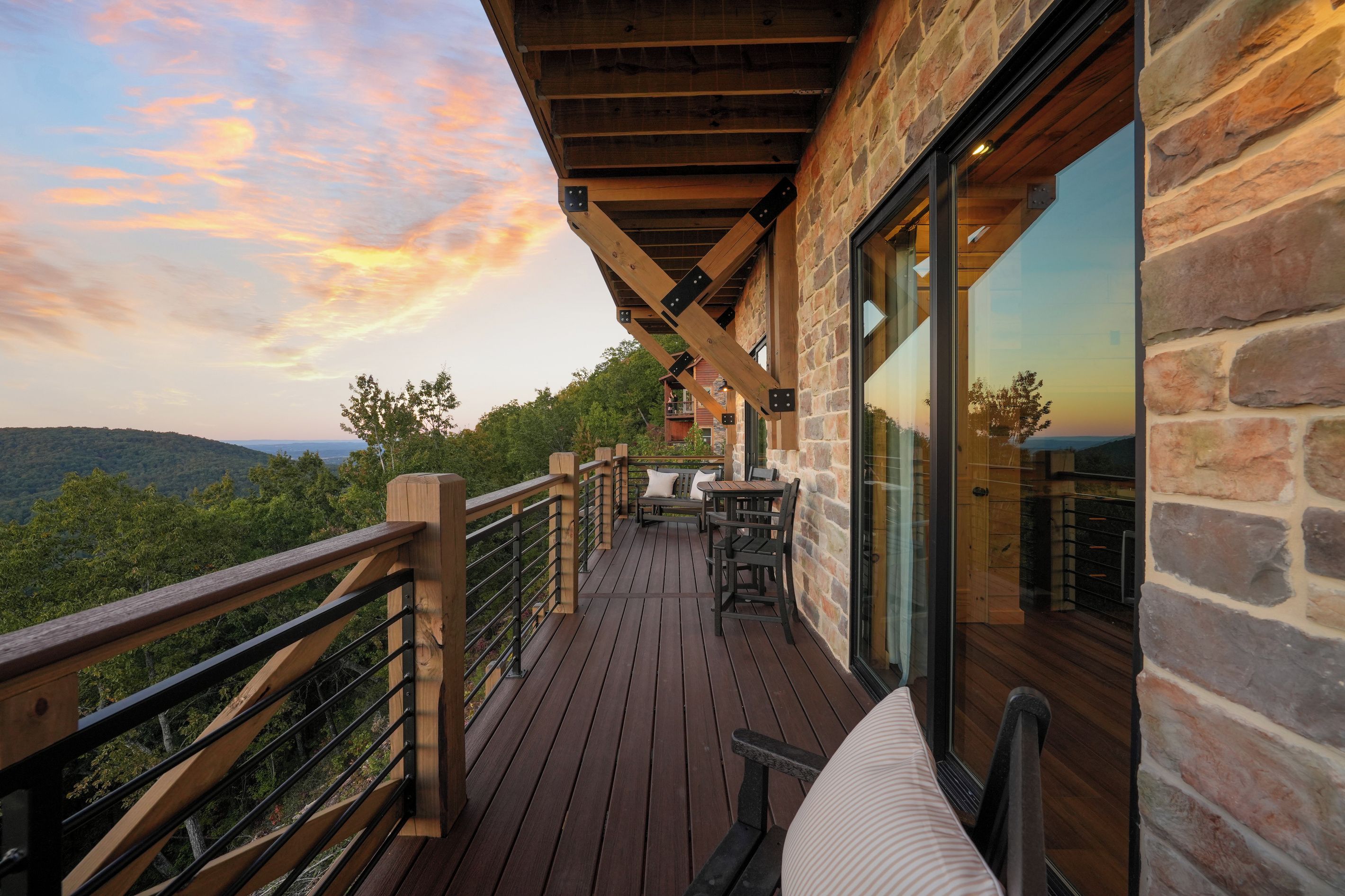 A wooden deck with outdoor seating, a stone wall, and a view of the landscape.