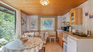 A cozy kitchen with wooden cabinets, a dining table with floral tablecloth, and a window with a view of greenery.