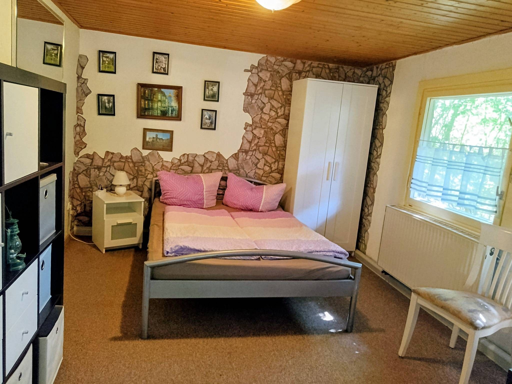 Ein Schlafzimmer mit Bett, Nachttisch, Kleiderschrank, Stuhl und Fenster mit Blick.