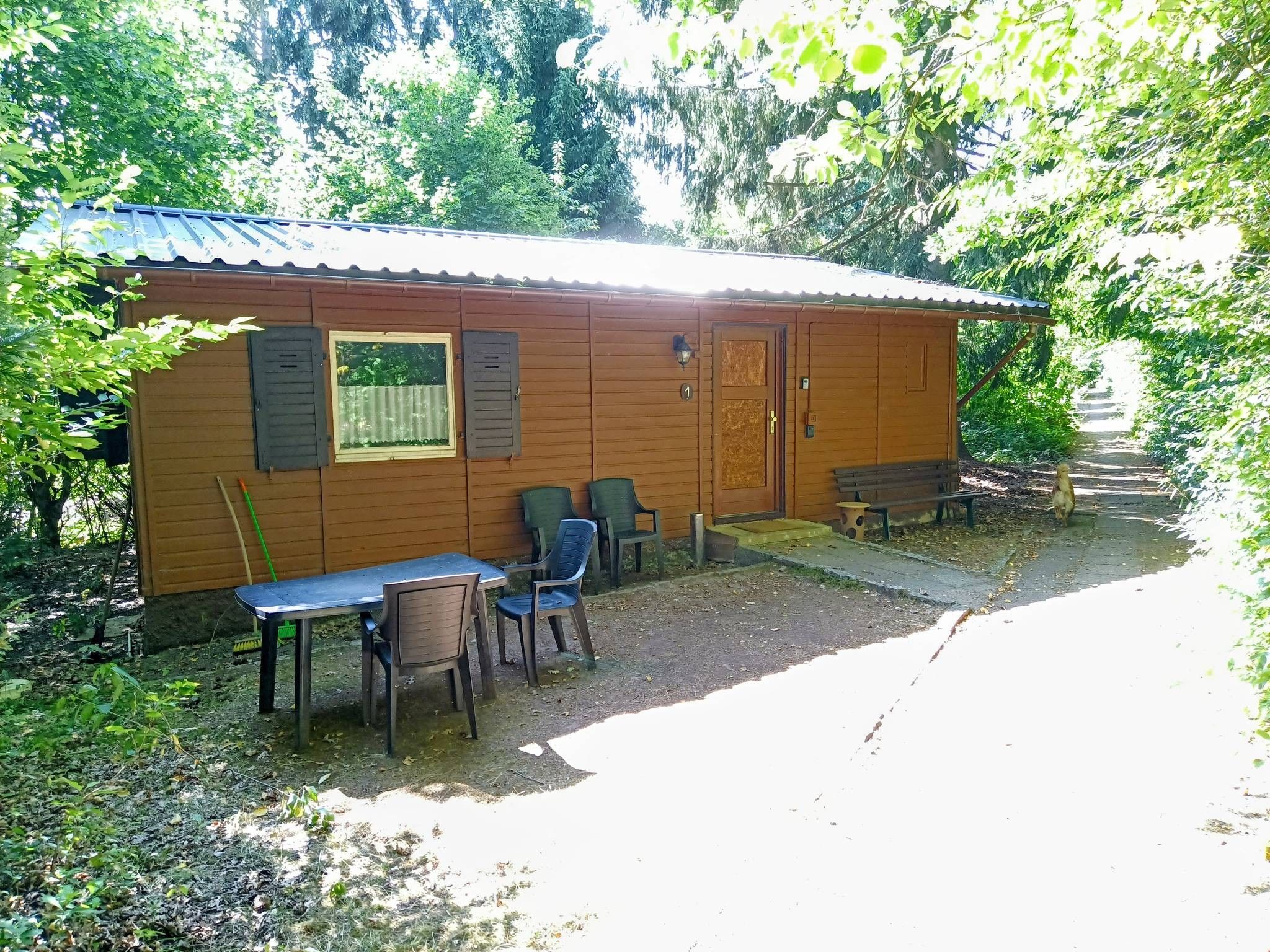 Eine kleine Holzhütte mit einer Tür, einem Fenster und einem Tisch mit Stühlen davor.