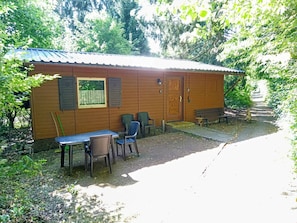 Una pequeña cabaña de madera con una puerta, una ventana y una mesa con sillas afuera.