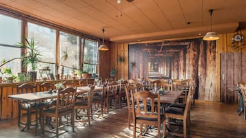 Een restaurant met houten tafels en stoelen, grote ramen en een plafondventilator.
