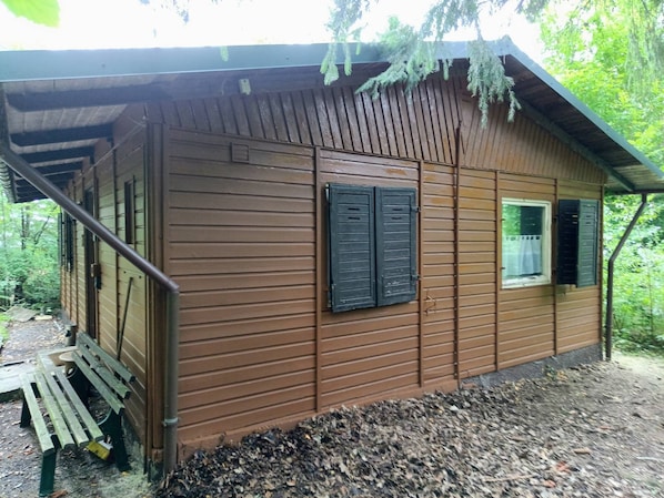 Una cabaña de madera con un porche, una ventana con contraventanas y un banco afuera.