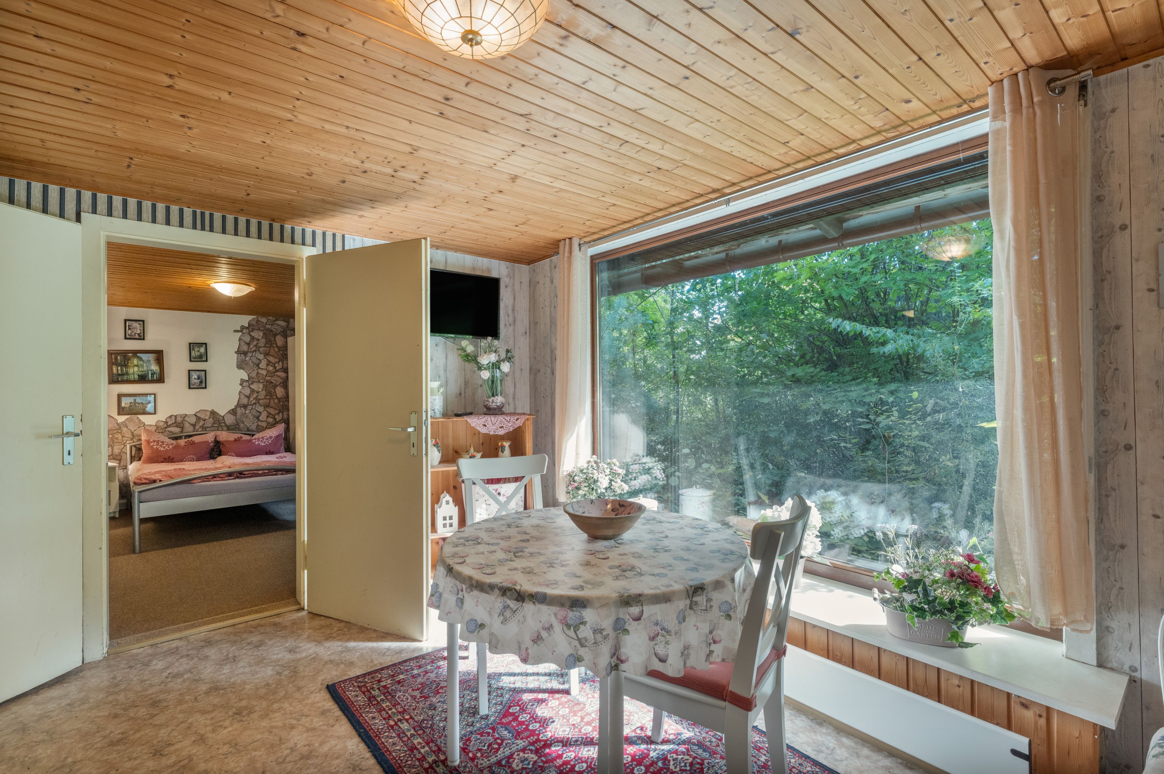 Una stanza con un letto, un tavolo con sedie, una televisione e un'ampia finestra vista sul verde.