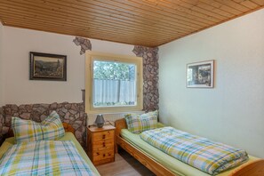 Une chambre avec deux lits, une fenêtre, une lampe et une commode.