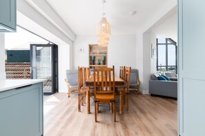 A modern dining area with a wooden table and chairs, a hanging light fixture, and a view through a glass door. - Sunset Beach (Croyde)