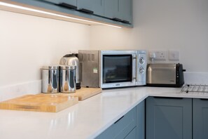 A kitchen with a microwave, toaster, and stainless steel containers on the counter. - Sunset Beach (Croyde)