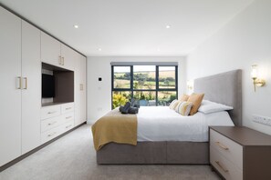 Une chambre avec une grande fenêtre, un lit, une télévision et une armoire.