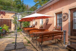 Ein Außenbereich mit Holzbänken und Tischen, Sonnenschirmen und einem rustikalen Gebäude mit einem an der Wand befestigten Rad.