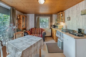 Ein gemütliches Blockhaushaus-Interieur mit Esstisch, einer Couch, einer Küchenzeile mit Herd und einem Fenster mit Vorhängen.