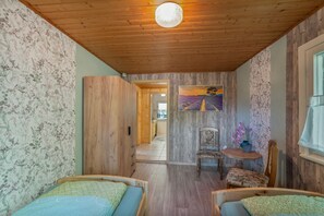 Una habitación con paredes y techo de madera, una cama, una silla, una mesita y un cuadro en la pared.