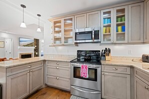 A kitchen with a stainless steel stove, microwave, and a built-in oven. There are wooden cabinets and a countertop with a knife block. - Kiawah Exclusives | 33 Inlet Cove (Kiawah Island)