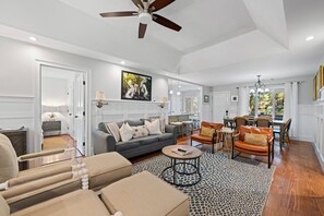 A spacious living room with a grey sofa, a coffee table, and a dining area with wooden chairs. - Kiawah Exclusives | 33 Inlet Cove (Kiawah Island)