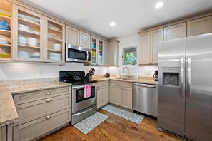 A modern kitchen with stainless steel appliances, wooden cabinets, and a window providing natural light. - Kiawah Exclusives | 33 Inlet Cove (Kiawah Island)