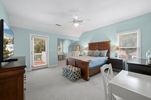 Ein Schlafzimmer mit Bett, Schreibtisch, Stuhl, Fenster mit Jalousien, Deckenventilator und Blick auf den Strand.