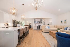 A modern kitchen with a central island, bar seating, and a dining area with a sofa and coffee table.