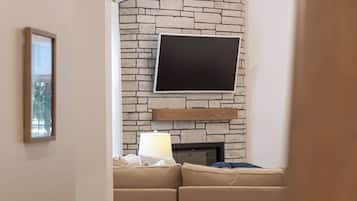 A living room with a stone wall, a flat-screen TV mounted above a fireplace, a sofa with cushions, and a lamp on a side table.