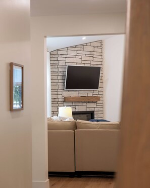 A living room with a stone wall, a flat-screen TV mounted above a fireplace, a sofa with cushions, and a lamp on a side table.