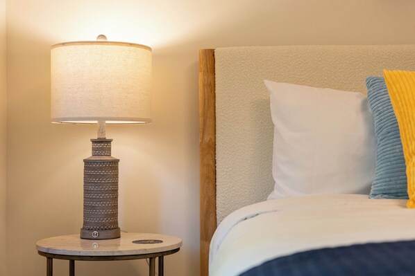 A bed with a headboard, a round table with a lamp, and a wall.