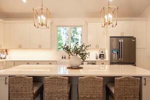 A kitchen with a large island, two pendant lights, and a refrigerator.
